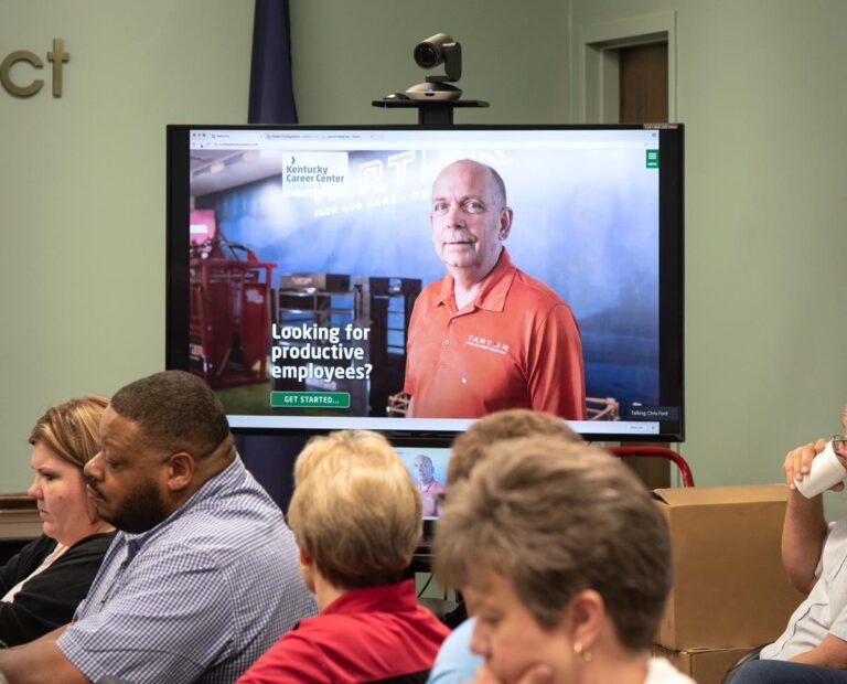large TV and webcam camera behind people at a meeting