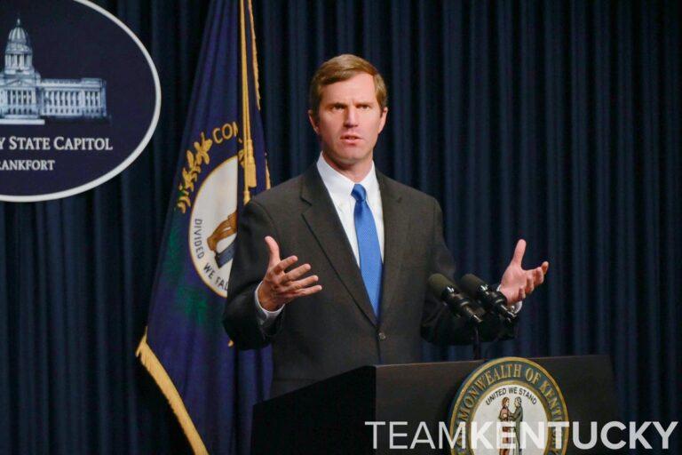 Man speaking at a podium with Kentucky flag in the backgrournd